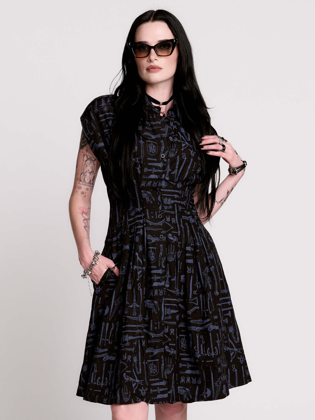 a button-front shirt dress featuring a striking medieval-inspired print with weaponry and macabre motifs.
