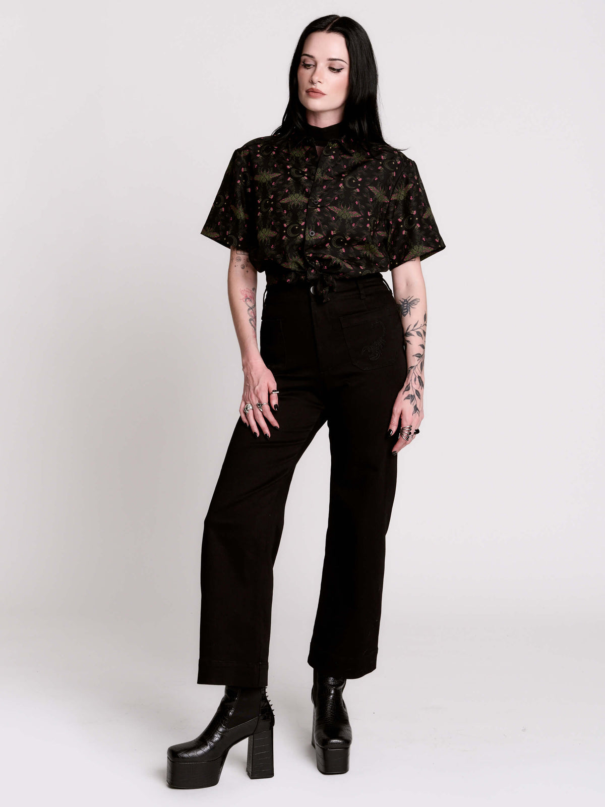 a black short-sleeve button-up shirt with a dark green and pink occult-style pattern.