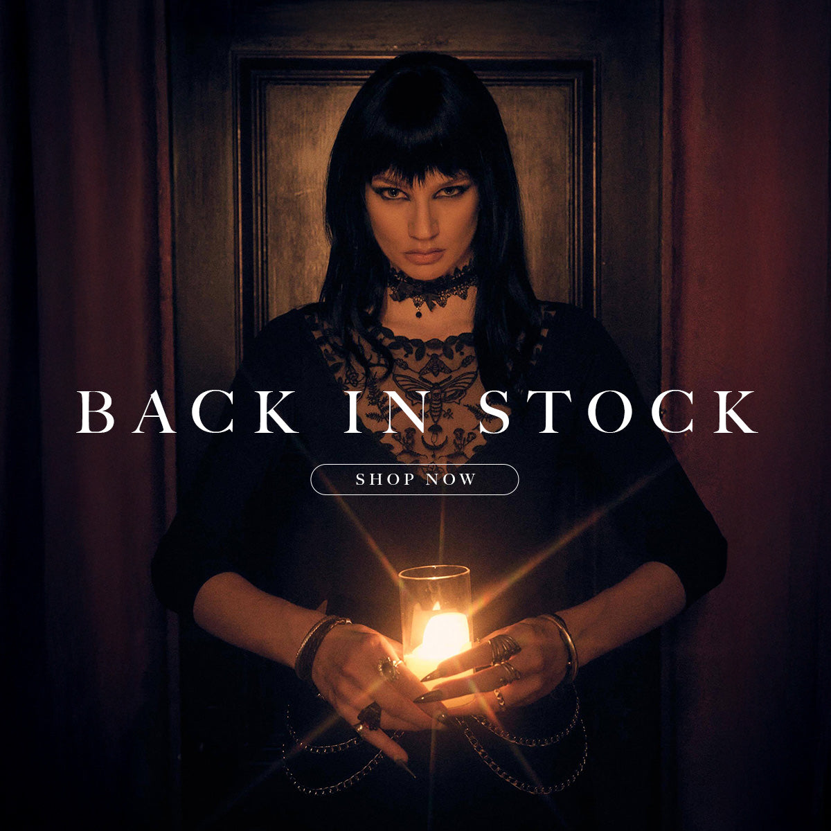 Woman holding a lit candle with text 'Back in Stock' and 'Shop Now' in a dark setting.