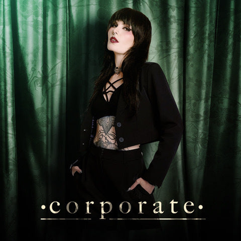 Person wearing a black outfit with tattoos against a green curtain backdrop, with 'corporate' text at the bottom.