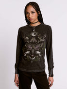Person wearing a black long-sleeve shirt with intricate designs on a plain background