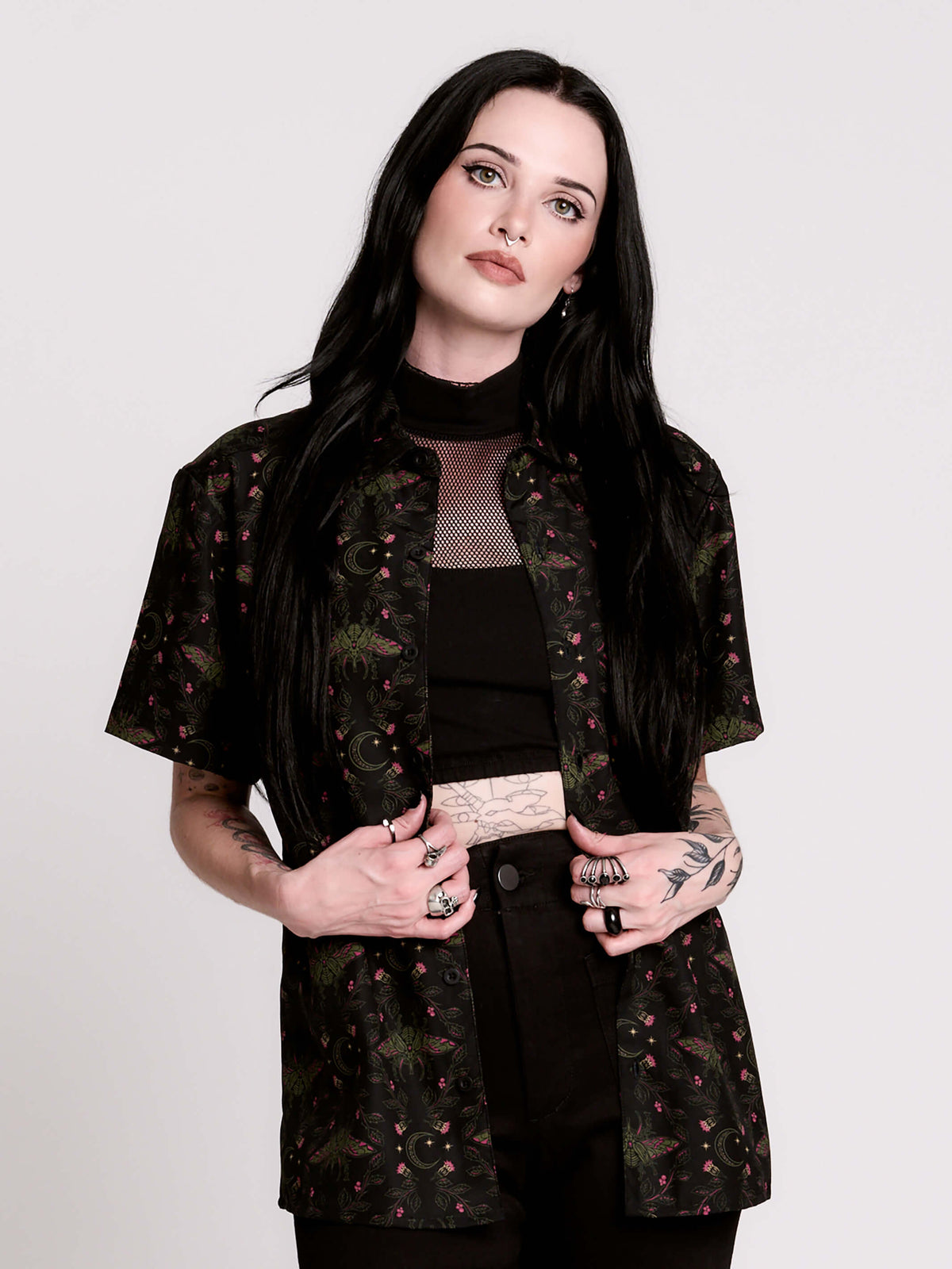 a black short-sleeve button-up shirt with a dark green and pink occult-style pattern.